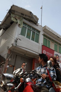A man rides a motorcycle with a woman past a house with a collapsed roof in Lushan county on April 20. Photo: Simon Song