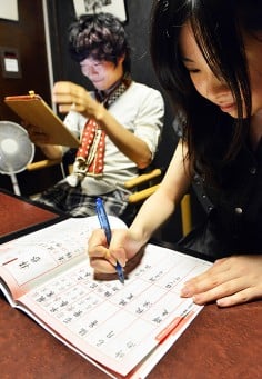 Akihiro Matsumura (left) uses his tablet, while his friend practices writing Chinese characters. Photo: AFP