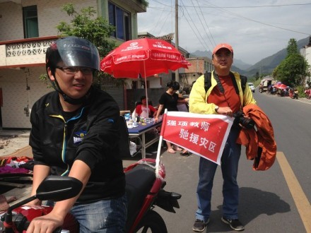 A local teacher surnamed Lai, left, sits on a bike with a banner on the rear seat reading 'tough teachers riding to help the disaster zone'. Photo: Simon Song