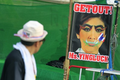 A Thai anti-government protester walks past a poster against Prime Minister Yingluck Shinawatra. Photo: EPA