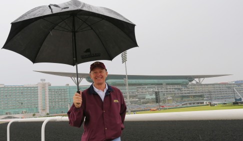 Hong Kong trainer John Moore shelters from unexpected rain at the Meydan track in Dubai on Wednesday. Photo: Kenneth Chan