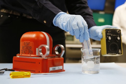 Erin Gormley, aerospace engineer at NTSB demonstrates an underwater locator beacon, removed from a sample flight recorder, left, to show how it emits a sound during a news media tour of the NTSB Vehicle Recorder Laboratory in Washington on Friday. Photo: AP