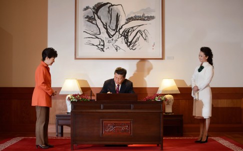 China's President Xi Jinping (centre) signs a guest book as his wife Peng Liyuan (right) watches, prior to attending a summit meeting with his South Korean counterpart Park Geun-Hye (left) at the Blue House in Seoul. Photo: AFP