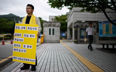 An activist holding a placard reading "confess your sins, find the truth behind the sunken ferry" protests against the government response to the Sewol ferry, as he stands outside Gwangju district court on July 8. Photo: AFP