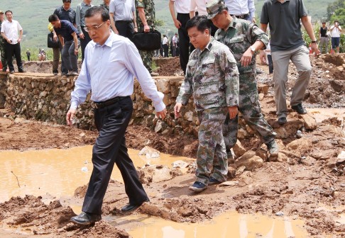 Li Keqiang (left) walks through flooded areas as he visits the site of the Yunnan earthquake that killed 398 people, as of the latest toll. Photo: Xinhua