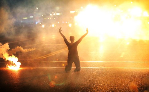 A woman kneels down in the street amid tear gas. Photo: AFP