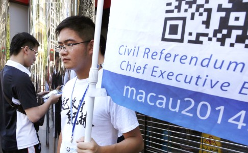 A man votes on a tablet next to a volunteer with a banner promoting informal civil referendum in Macau on Sunday. Photo: AP