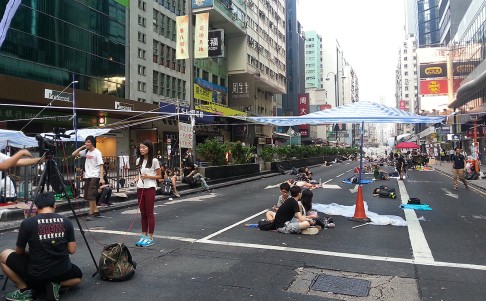 Protesters sleep while a TV reporters make preparations for preparing for a live broadcast from Mong Kok