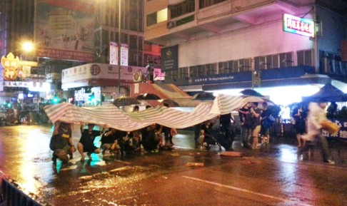 Protesters take cover under a tarp. Photo: Danny Mok