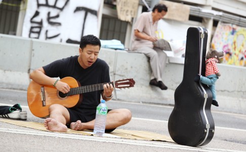 A man with a guitar sings in Admiralty. A Lufsig toy, used to mock CY Leung, hangs from his guitar case. Photo: Dickson Lee