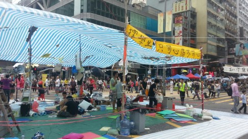 Pedestrians walk around the protest camp in Mong Kok, which is clearly demarcated with blankets and tarps for flooring, a canopy, and even small furniture. Photo: Thomas Chan