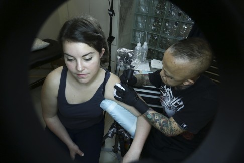 Kin Liu etches a flower on reporter Sarah Karacs' arm.