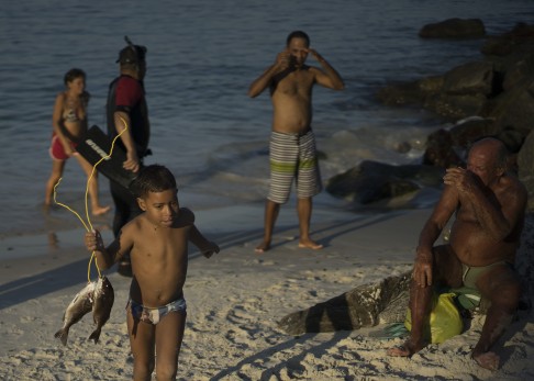 In this July 12, 2015 photo, a boy walks with his father's catch of the day from the Marina da Gloria, in Rio de Janeiro, Brazil. The head of Rio's Infectious Diseases Society said contaminated waters in beaches and lakes has led to "endemic" public health woes among Brazilians, primarily infectious diarrhea in children. By adolescence, he said, people in Rio have been so exposed to the viruses in the water their bodies build up antibodies. But foreign athletes and tourists won’t have that protection. (AP Photo/Leo Correa)