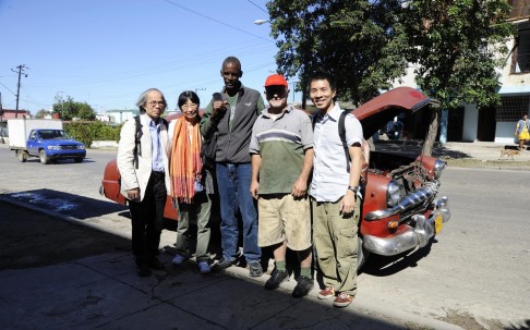 Louie (left) and friends stand in front of a vintage taxi in Havana. 