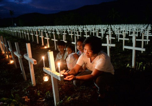 A woman, accompanied by her young family members, writes the name of a loved one on a cross at a mass graveyard for victims. Photo: AFP