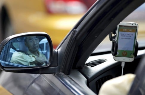 A taxi driver is reflected in a side mirror as he uses the Didi Chuxing car-hailing application in Beijing.