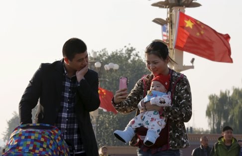 A couple take pictures with their baby at the Tiananmen Gate in Beijing. Photo: Reuters