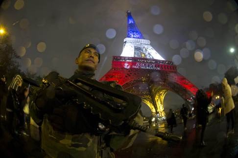 A soldier enforces France's national security alert system at the Eiffel Tower, which is illuminated with the colours of the national flag in tribute to the victims. Photo: AFP