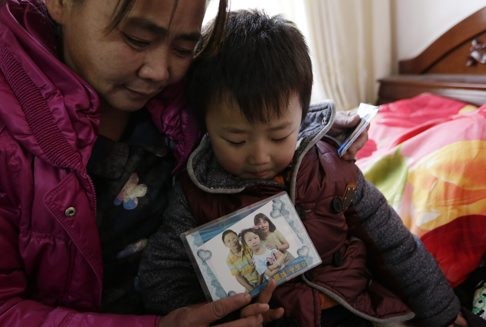 Migrant worker Mei Qiuyu with her five-year-old son, holding a photo of herself, her husband and 12-year-old daughter in their home in Daxing district of Beijing. Mei is petitioning for her two children to be granted a hukou. Photo: EPA