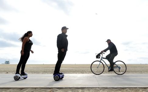 Michael Tran and Katie Rodriguez pass a cyclist on their hoverboards on the Venice Beach Boardwalk in California. Photo: AFP