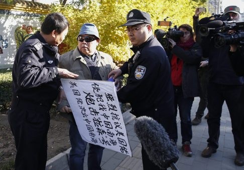 A protester holding a sign that reads “Strongly protest against US encroachment on South China Sea. Attack USS Lassen. Americans get off South China Sea” is confronted by two Chinese police officers outside the US Embassy in Beijing. Photo: EPA