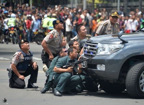 Indonesian police take cover behind a vehicle as they pursue suspects after a series of blasts hit Jakarta. Photo: AFP