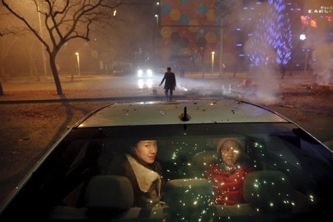 A girl and a woman sit inside the car as firecrackers and fireworks explode celebrating the start of the Chinese Lunar New Year of Monkey in Beijing just before midnight February 7, 2016. Photo: Reuters