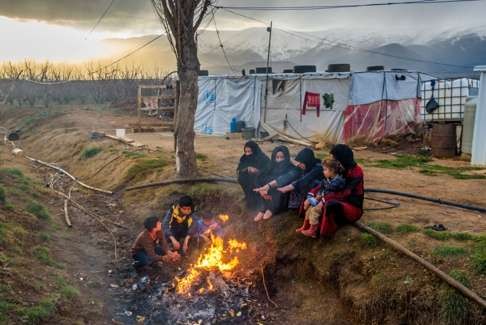 A Syrian refugee family in Lebanon sits by a fire in a ditch in front of their tents, burning garbage – mostly plastic – to stay warm. Photo: World Vision