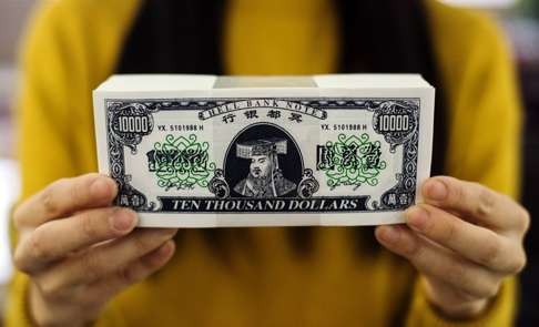 A Chinese worker holds up lookalike US dollars printed as “spirit money”, intended as burnt offerings for ancestors. In the real world, the US not only needs to tap China’s foreign currency reserves, but it also needs access to its vast market. Photo: AFP