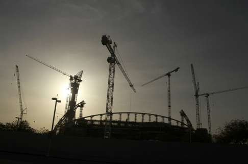 Cranes are silhouetted against the grey sky at the Khalifa International Stadium. Photo: Reuters