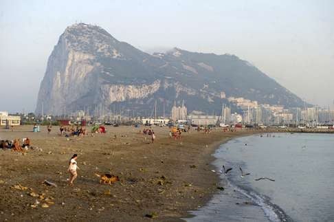 People walk on a Spanish beach with a clear view of the rock of Gibraltar. Photo: AP