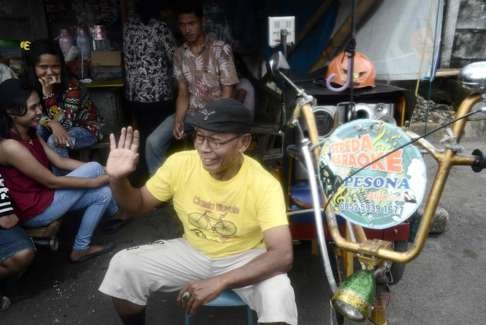 Rudi Hantoro sitting beside his karaoke rickshaw. Photo: AFP