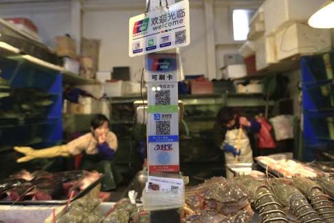 Placards on a seafood stall show various non-cash ways to pay which include UnionPay cards, and QR codes of WeChat and Alipay at a market in Beijing, China. Photo: EPA