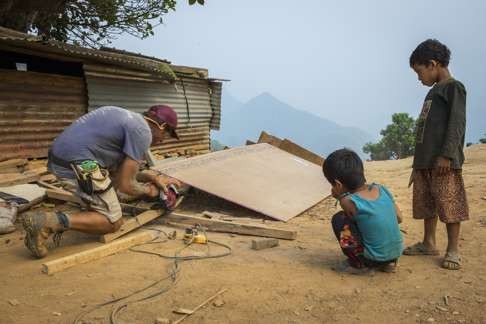 Village children watch as a volunteer works on site in Nuwakot, where All Hands Volunteers and Room to Read are partnering to build earthquake-safe schools. According to Room to Read, some 47,000 classrooms in Nepal were damaged or destroyed.