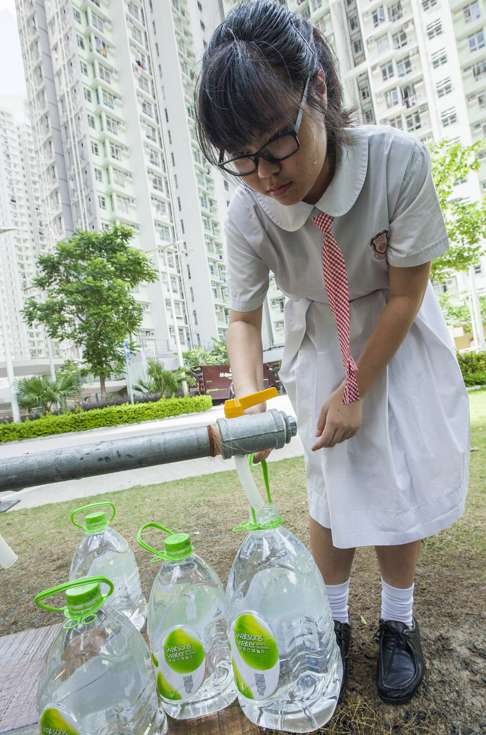 A girl who lives in the Kai Ching Estate fills up containers of drinking water from a temporary standpipe in the street. Photo: EPA