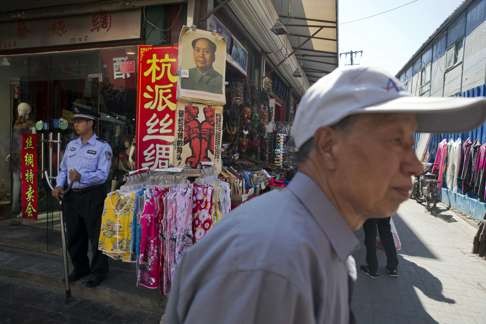 A man walks past a security guard holding a prong for restraining attackers near a poster of Mao Zedong and Cultural Revolution banners at a curio market in Beijing. Photo: AP