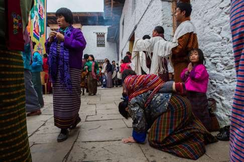A Bhutanese mother prostrates herself in front of a giant Buddhist tapestry called a Thongdrel, as others wait to enter the main prayer hall of the temple at the Simtokha Dzong in Simtokha, Bhutan. The country imposes a hefty daily surcharge on tourists to limit numbers. Photo: AFP