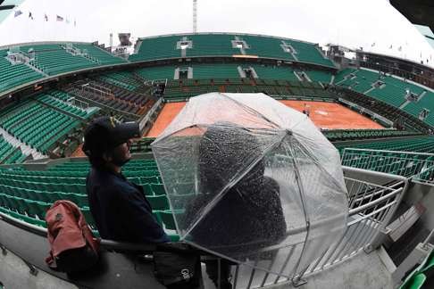 A spectator stands under an umbrella in the empty stands of Philippe Chatrier court. Photo: AFP