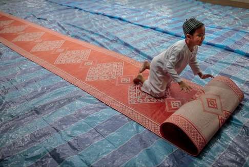 A young Malay boy unrolls a mat in preparation for evening prayers at a residential block in Singapore, during the Islamic holy month of Ramadan. The Singaporean experience reveals the use of Tamil, Malay, English and Mandarin coexisting in society. Photo: EPA