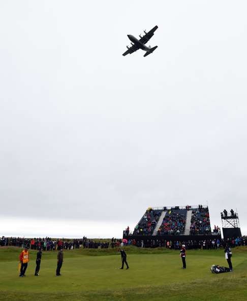 A Lockheed C-130 Hercules flies over the 15th green as Sweden's Henrik Stenson, US golfer Zach Johnson and Australia's Adam Scott putt during their second rounds. / AFP PHOTO