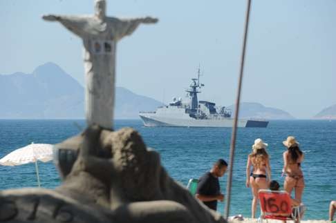 People enjoy the day at Copacabana beach as a warship patrols the coast. Photo: AFP
