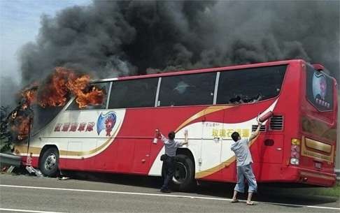 A policeman and a bystander try to break the windows of the burning tour bus on July 19. Photo: AP