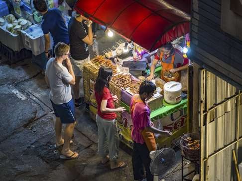 A tourist looking at grilled meats and sausages at a food stall on Sukhumvit Soi 38, one of the most famous street food areas in Bangkok. Photo: Jack Kurtz/ZUMA