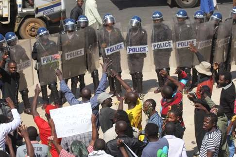 Zimbabwean protestors hold flowers and banners as police stand by. Photo: AP