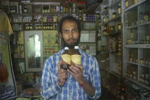 Shop owner Ashok Chandra holds up Baba Ramdev’s distilled cow urine in Bhimtal, northern India. Photo: Amrit Dhillon