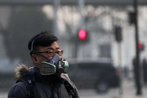 A man wearing a mask walks on a street in Beijing as the capital of China is blanked by smog on Friday. Photo: AP