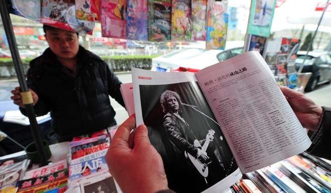 A customer looks at a magazine, which features a photograph of American singer Bob Dylan performing, at a newspaper kiosk in Beijing. Photo: AFP