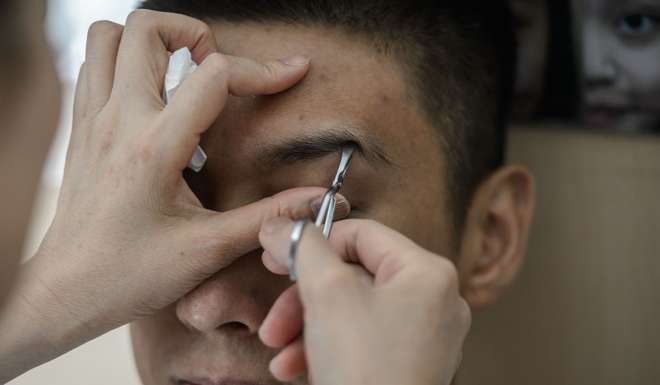 Customer Edward Lam has his eyebrows plucked by Li Chau-jing. Photo: AFP