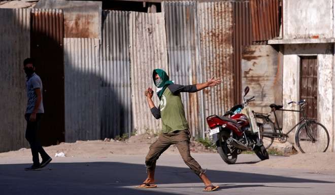 A demonstrator hurls a stone towards Indian policemen during a protest in Srinagar, against the recent killings in Kashmir region. Photo: Reuters