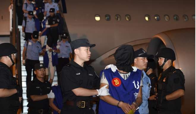 Hooded fraud suspects are escorted off a plane by Chinese police at Lukou International Airport in Nanjing, Jiangsu province, after being deported from Cambodia this month. Cambodia has deported 13 Taiwanese and 50 Chinese suspects to China. Photo: Xinhua via AP
